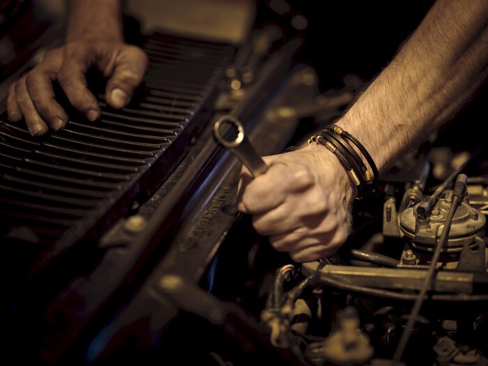 Hands working on a vehicle engine with a wrench