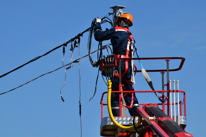Utility worker in a hard hat and harness repairing overhead power lines